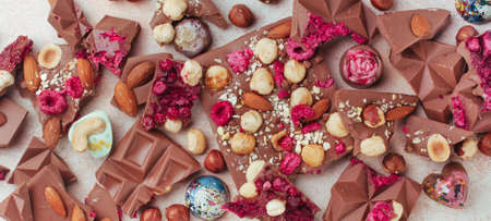 Broken bars of milk chocolate with nuts and sublimated berries and chocolate candies on textured...