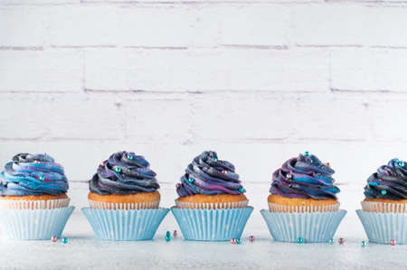 Vanilla cupcakes with galaxy dark whipped cream on brick background with blank space for textの写真素材