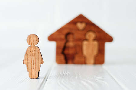 Wooden female figure in front of house on white background as symbol of problems in family relationships. Focus on female figure, blank space for text.の写真素材