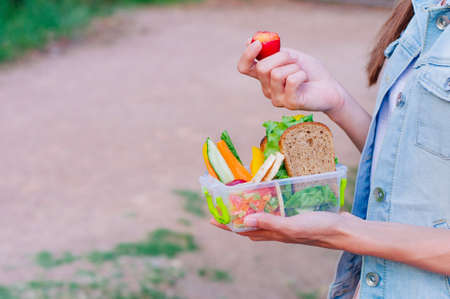 Healthy food concept: Young woman eating from lunch box filled with sandwich, crispbreads, fruits and vegetables outdoor; selective focusの写真素材