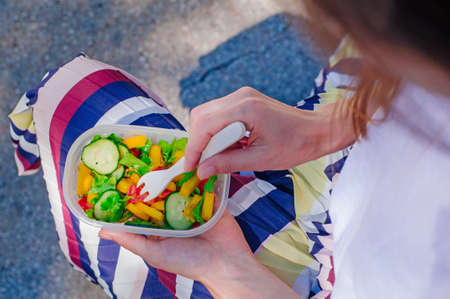 Healthy food concept: Young woman eating from lunch box filled with salad outdoor. Selective focus