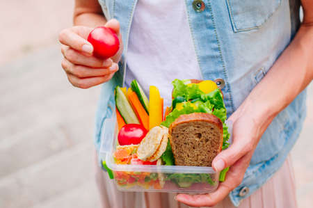 Healthy food concept: Young woman eating from lunch box filled with sandwich, crispbreads, fruits and vegetables outdoor; selective focusの写真素材