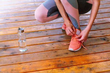 Young woman in sportswear tying her sneaker shoe on wooden background with copy space; selective...