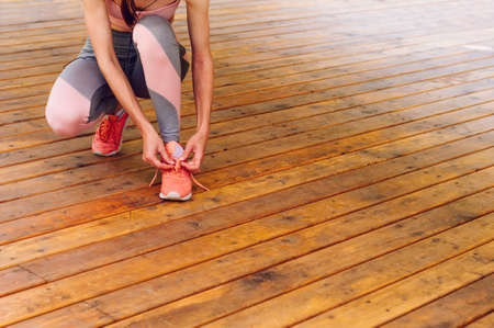 Young woman tying her sneaker shoe on wooden background with copy space; selective focusの写真素材