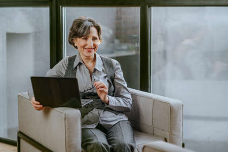 Mature business woman talking with somebody using laptopの写真素材