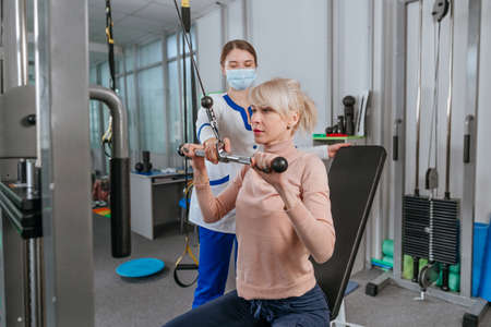 Female doctor rehabilitologist working with female patient on the special rehabilitation device