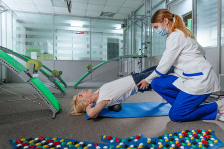 Female doctor rehabilitologist showing female patient exercises at rehabilitation center gymの写真素材