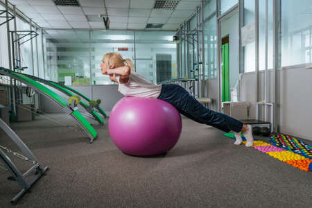 Young woman doing exercises with ball for recovery at rehabilitation center gymの写真素材