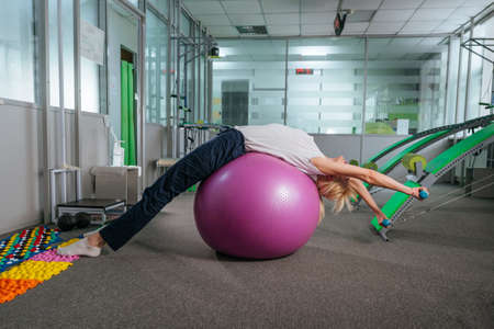 Young woman doing exercises with ball for recovery at rehabilitation center gymの写真素材