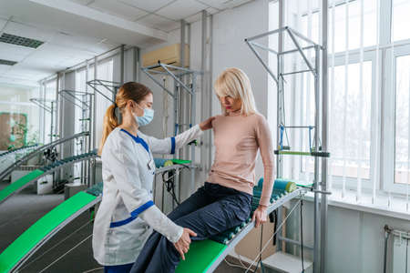 Female doctor rehabilitologist working with female patient on the special rehabilitation device