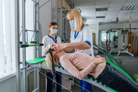 Female doctor rehabilitologist working with female patient on the special rehabilitation device