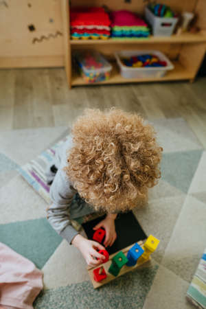 Preschool students sorting wooden geometric shapes sittings on the floorの写真素材