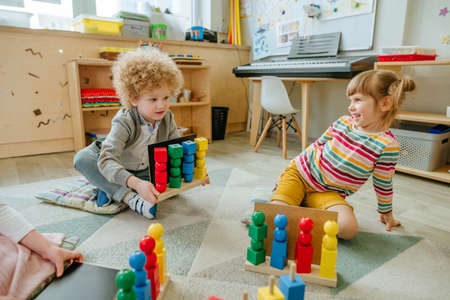Preschool students sorting wooden geometric shapes sittings on the floorの写真素材