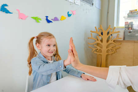 Happy little girl giving high five to her teacher after good work at lessonの写真素材