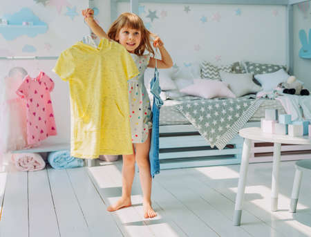 Beautiful little girl choosing a dress in the kids roomの写真素材