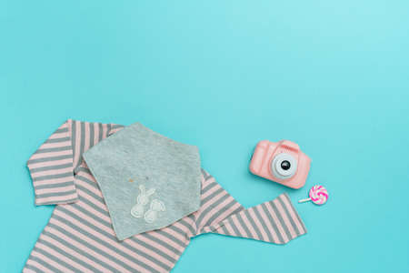 Kids clothes background. Romper and bib from organic cotton and toy photocamera on blue background with blank space for text. Top view, flat lay.の写真素材