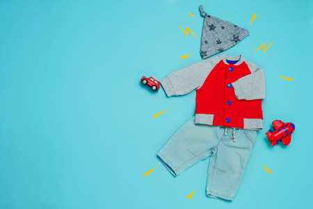 Baby clothes and accessories background. Boy's jacket, jeans and hat with toys over blue background with blank space for text. Top view, flat lay.の写真素材