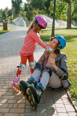 Little cute girl helping her grandmother wearing helmet prepairing for roller skatingの写真素材