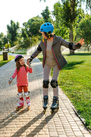 Active happy grandmother and granddaughter having fun time together during roller skatingの写真素材