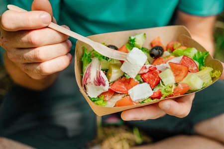 Healthy food concept. Closeup of man eating fresh mixed vegetables. Vegetable salad in the brown kraft paper food container. Selective focus.の写真素材