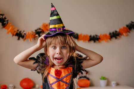 Portrait of little girl dressed Halloween witch costume and hat in decorated room. Selective focus on the face.の写真素材
