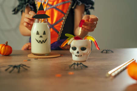 Close up of little girl dressed Halloween witch costume sitting at the table with milkshakeの写真素材