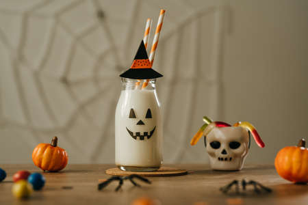 Idea for kids Halloween party table. Glass bottle of milk cocktail decorated with jack-o-lantern face and hat.の写真素材