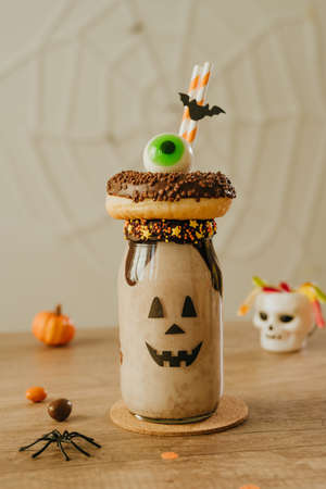 Idea for kids Halloween party table. Freak Monster shake decorated with chocolate donut and marmelade eye. Jack-o-lantern face on the jar. Copy space for text.の写真素材