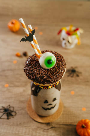 Idea for kids Halloween party table. Freak Monster shake decorated with chocolate donut and marmelade eye. Jack-o-lantern face on the jar. Copy space for text.の写真素材