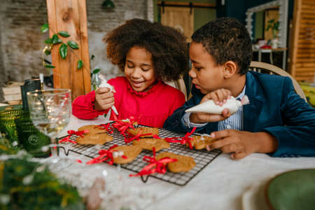 Sister and brother decorating Christmas gingerbreads with ribbons at homeの写真素材