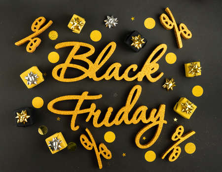 Golden inscription Black Friday on dark background with gift present boxes and confetti. Top view, flat lay.の写真素材