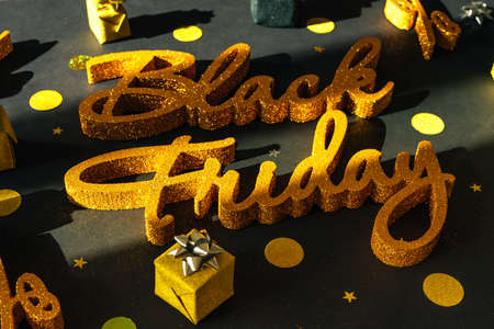 Golden inscription Black Friday on dark background with gift present boxes and confetti. Top view, sunlight.の写真素材