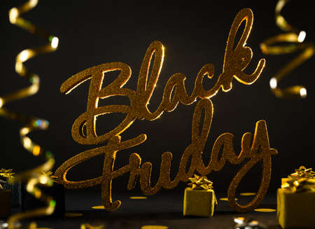 Golden inscription Black Friday on dark background with gift present boxes and confetti.の写真素材