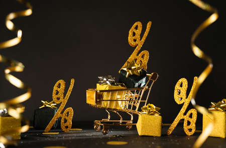 Golden toy shopping cart on dark background with gift present boxes and confetti. Black Friday concept.の写真素材