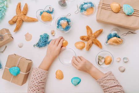 Close up of girl's hands filling ornaments with seashell and moss on white background. Christmas decor idea with using natural materials. Top view, flat lay.の写真素材