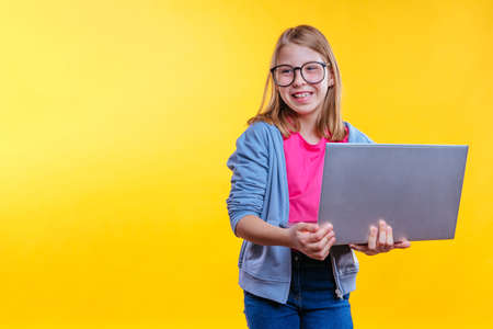 Happy blonde hair schoolgirl with eye glasses holding laptop on yellow background with blank space for textの写真素材