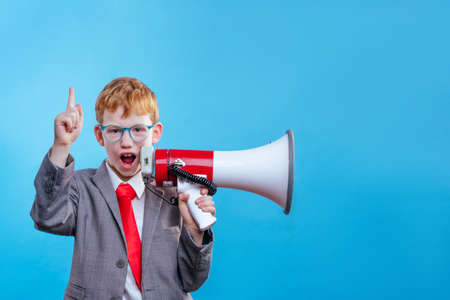 Funny red hair boy young businessman wearing suit and tie with eye glasses on blue background with blank space for textの写真素材