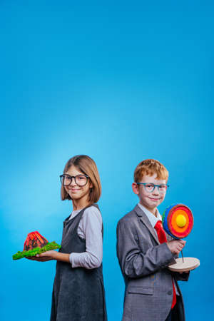 Two schoolchildren with eye glasses holding their scientific projects volcano and section of the Earth on blue background with blank space for textの写真素材