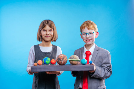 Two schoolchildren with eye glasses holding their scientific projects volcano and section of the Earthの写真素材
