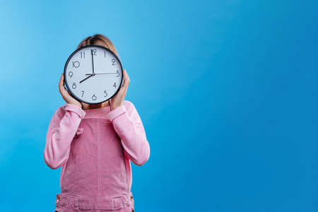 Little girl holding clock on blue background with blank space for text. Horizontal panoramic banner.の写真素材