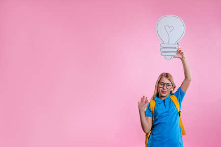 Little girl wearing backpack holding paper sketch lamp on pink background