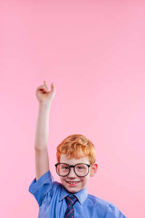 Little boy wearing eye glasses and tie pointing up on pink background with blank space for text.の写真素材