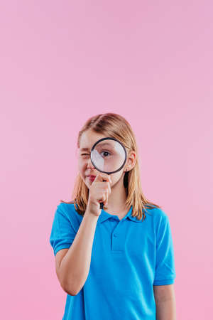 Schoolgirl looking throw magnifying glass on pink background with blank space for textの写真素材