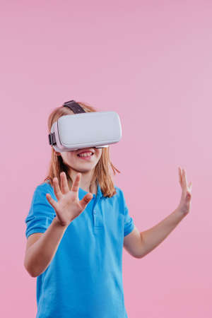 Teenager girl wearing virtual reality device. Studio portrait on pink background with blank space...