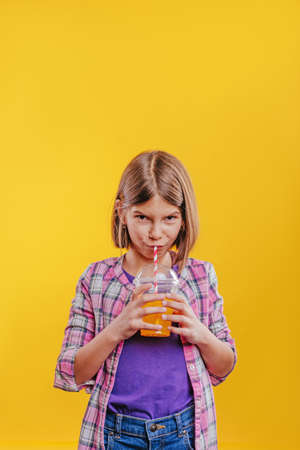Teenager girl drinking orange juice. Studio portrait on yellow background with blank space for text.の写真素材