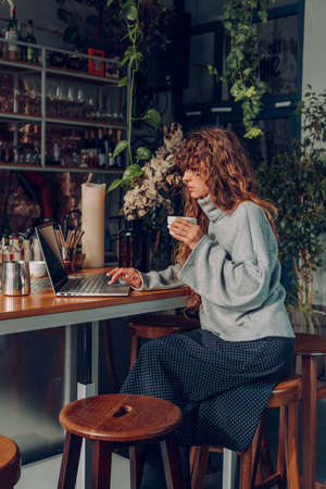 Business woman with curly hair working at the cafe remote office using laptop. Selective focus.