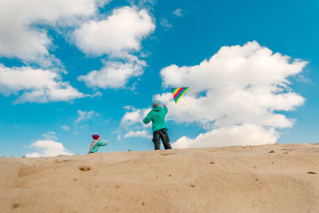 Father with his 5 years old daughter flying a kite on the sand beach. Happy family activities outdoor. Parenthood concept.の写真素材
