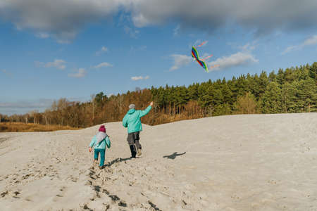 Father with his 5 years old daughter flying a kite on the sand beach. Happy family activities outdoor. Parenthood concept.の写真素材