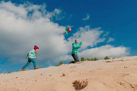 Father with his 5 years old daughter flying a kite on the sand beach. Happy family activities outdoor. Parenthood concept.の写真素材