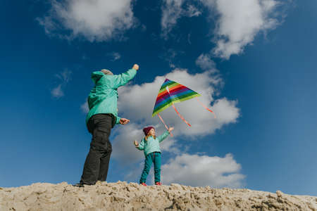 Father with his 5 years old daughter flying a kite on the sand beach. Happy family activities outdoor. Parenthood concept.の写真素材